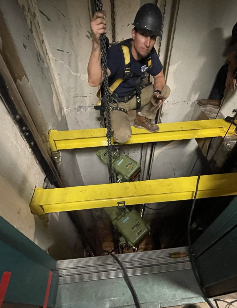 a man stands on supports running across an elevator shaft with LGH chain hoists